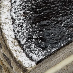 Macro shot of cake corner showing glossy black sesame glaze and sugar dusting