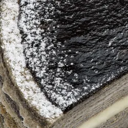 Macro shot of cake corner showing glossy black sesame glaze and sugar dusting