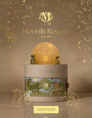 Lady M Mid-Autumn promo banner for the Moonlit Reverie Gift Set. Features a cylindrical gift box topped with two golden rabbit figurines and a glowing patterned moon globe, set against celestial gold line art. Text reads 'Limited Quantities', 'Moonlit Reverie Gift Set', and a 'SHOP MID-AUTUMN' button.