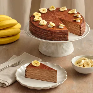 Chocolate Banana Mille Crêpes on a stand beside a sliced piece and fresh bananas