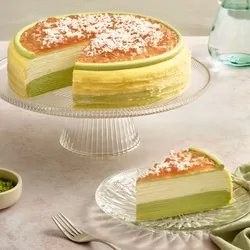 Coconut Matcha Mille Crêpes on a stand beside a sliced piece and matcha powder