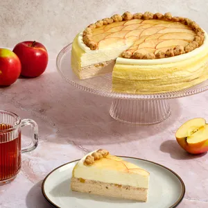 Apple Pie Mille Crêpes on a glass stand with a slice, red apples, and tea on pink stone