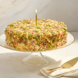 Lady M Birthday Cake 9" covered in colorful crêpefetti with a lit gold candle on a cake stand