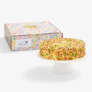 Lady M Birthday Cake 9" on a cake stand beside its colorful confetti-print gift box