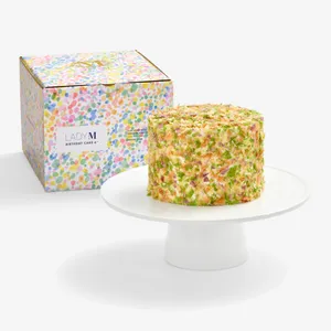 Lady M Birthday Cake 6" on a cake stand beside its colorful confetti-print gift box